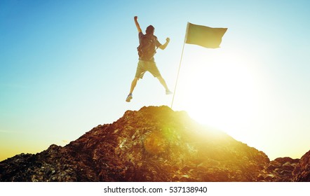 success, leadership, achievement and people concept - silhouette of young guy with flag on mountain top over sky and sun light background