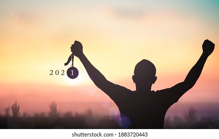 Success new year 2021 concept: Silhouette winner hand holding gold medal reward with text for 2021 against blurred sunset background - Shutterstock ID 1883720443