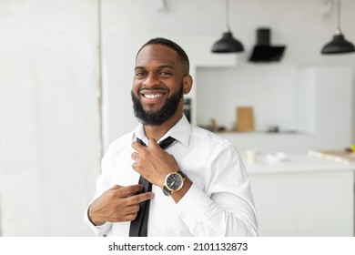 Success. Portrait Of Smiling Confident Young African American Business Man Adjusting Necktie At Home, Getting Ready For Work, Wearing White Shirt And Luxury Wrist Watch, Posing Looking At Camera