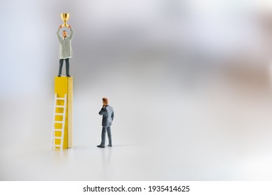 Success Story Of A Company Top Performer, Business Concept : Top Rank Sales Leader Raises A Gold Trophy Cup On A Pole With A Ladder, A Rival Stands Below And Thinking Of Ways To Beat This Competition