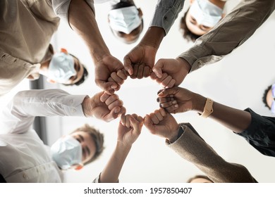 Success And Teamwork Concept. Below View Of Young Diverse Group Of Business People In Protective Medical Masks Making Fist Bump Standing In Circle. Workers Do Fist Pump Together Celebrating Good Deal