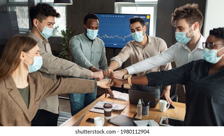 Success And Teamwork Concept. Portrait Of Diverse Group Of Businesspeople In Disposable Face Masks Making Fist Bump Above Table Standing At Office. Workers Do Fist Pump Together Celebrating Good Deal