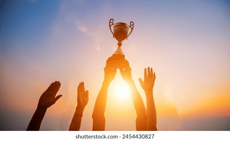 Success of teamwork, joint achievement of goal in business and life. Winning team is holding trophy in hands. Silhouettes of many hands in sunset. - Powered by Shutterstock