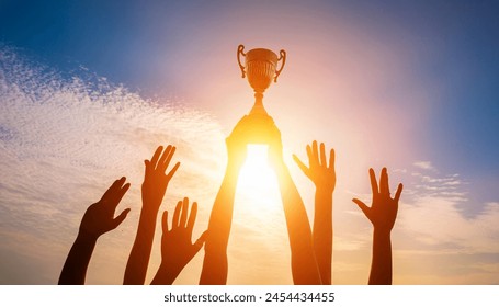 Success of teamwork, joint achievement of goal in business and life. Winning team is holding trophy in hands. Silhouettes of many hands in sunset. - Powered by Shutterstock