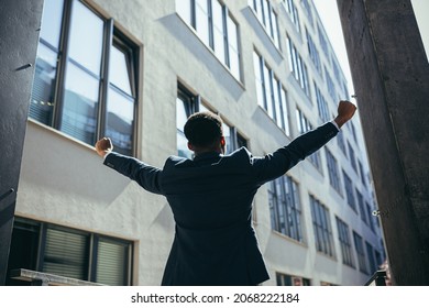 Successful african american businessman with arms up celebrating victory. Concept: success, career growth, victory, freedom. silhouette business man on the background a modern office building. outside - Powered by Shutterstock