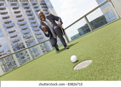 Successful African American Businessman Or Man In A Suit Playing Golf On A Corporate Putting Green On Roof Of A Skyscraper Office Building
