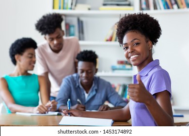 Successful African American Female Student Learning At Desk At School With Teacher And Group Of Students At Classroom