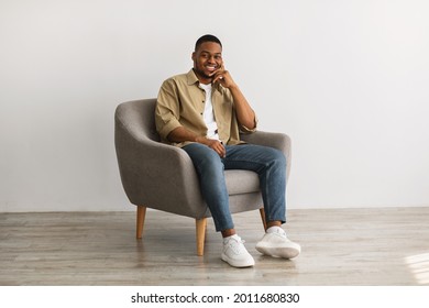 Successful African American Millennial Man Smiling To Camera Posing Sitting In Comfortable Chair Over Gray Wall Background Indoors. Young Male Relaxing At Home Concept. Full Length - Powered by Shutterstock