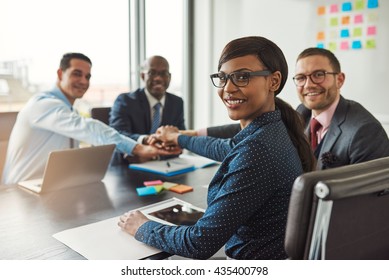 Successful African American team leader turning to smile at the camera as her multiracial team of executives links hands across the table