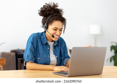 Successful African American woman in headset, office employee or call center worker sitting in a modern office talking, consulting client using video call, smile