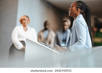 Successful African business woman engages with her audience while giving an inspiring speech at a professional conference. Colleagues listen intently in a modern corporate setting. - Powered by Shutterstock