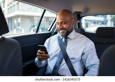 Successful african businessman working on phone witting in car. Mature smiling business man in formal using smartphone while sitting on back seat of business car. Happy senior man reading email. - Powered by Shutterstock