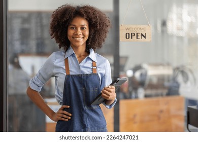 Successful african woman in apron standing coffee shop door. Happy small business owner holding tablet and working. Smiling portrait of SME entrepreneur seller business standing with copy space. - Powered by Shutterstock