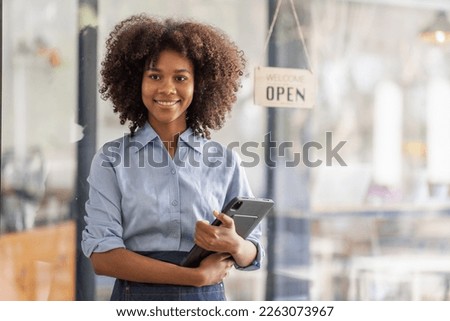 Successful african woman in apron standing coffee shop door. Happy small business owner holding tablet and working. Smiling portrait of SME entrepreneur seller business standing with copy space.