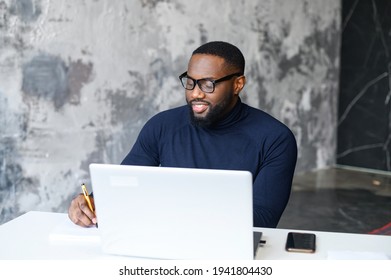 Successful African-American Male Employee Using The Laptop For Work At Modern Loft Office, Watching Webinars And Taking Notes With A Pen, Working On A New Project, Businessman Plans Tasks For The Week