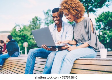 Successful Afro American Best Friends Dressed In Casual Clothing Joking And Laughing During Using Modern Device Sitting On Bench.Happy Man And Woman Watching Funny Video In Website On Laptop Computer