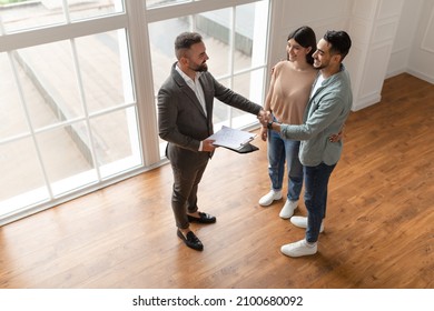 Successful Agreement, Real Estate, Home Buying Contract Concept. Happy Smiling Millennial Buyers Shaking Hand With Professional Realtor Agent In New Apartment, Sealing A Deal Together, High Angle View