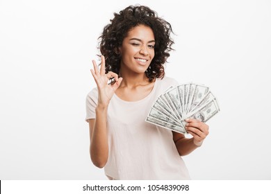 Successful American Woman With Curly Dark Hair Holding Fan Of Money Dollar Bills And Showing Ok Sign Isolated Over White Background