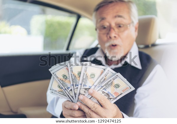 Successful Asian business Senior rich\
 man holding\
money US dollar bills in his car ,  concept business Stock trader\
player 
