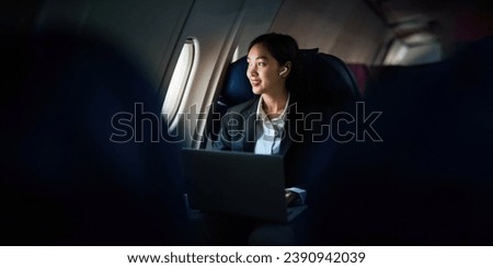 Successful Asian business woman, Business woman working in airplane cabin during flight on laptop computer listening to music with headphones