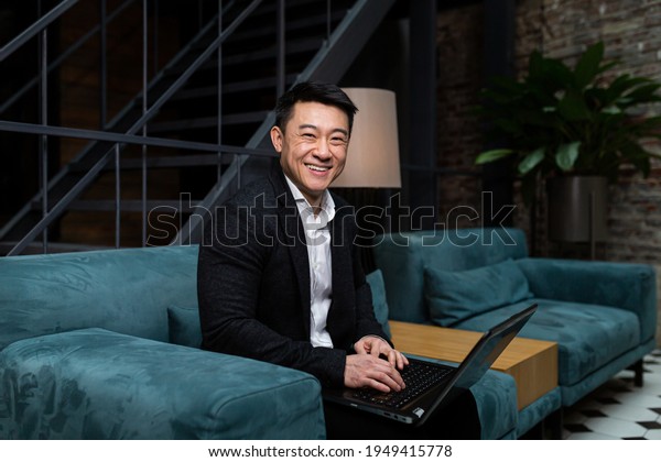 Successful Asian\
businessman, in a black business suit, works on a laptop, relaxes\
in a restaurant or hotel, and in a stylish office explains a new\
business strategy via video\
link