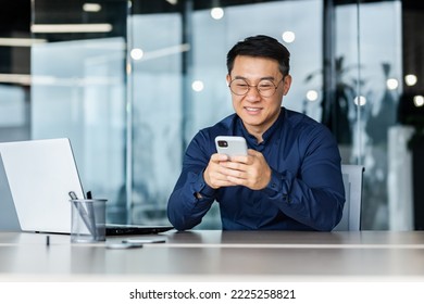 Successful Asian businessman working inside modern office building, man smiling and happy using smartphone to browse online pages, man in shirt and glasses with laptop. - Powered by Shutterstock