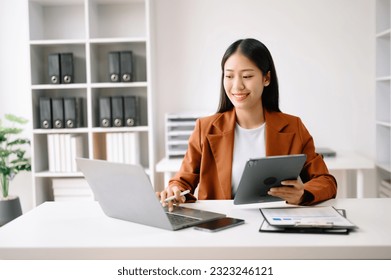 Successful Asian Businesswoman Analyzing Finance on Tablet and Laptop at modern Office Desk tax, report, accounting, statistics, and analytical research concept