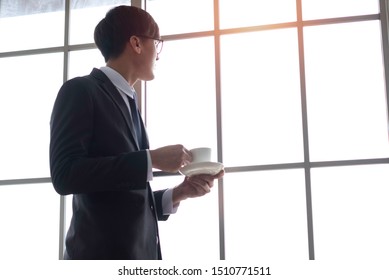 Successful Asian Entrepreneur Standing In Office Drinking Coffee. 