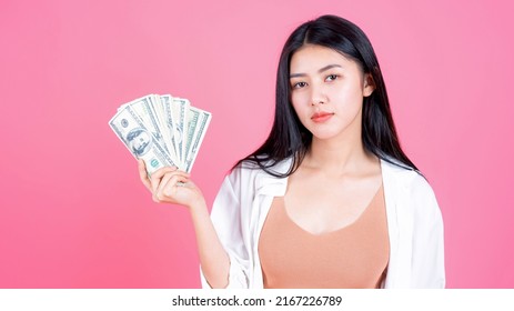 Successful Beautiful Asian Business Young Woman Holding Money US Dollar Bills In Hand On Pink Background , Business Concept