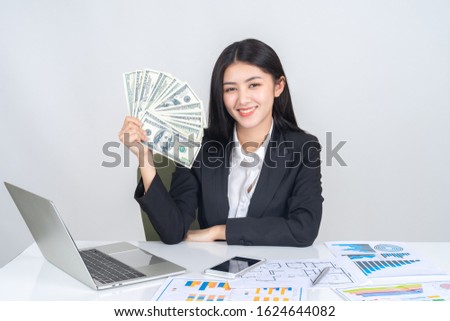 Successful beautiful Asian business young woman holding money US dollar bills in hand on office desk, business concept