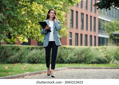 Successful Beautiful Business Woman In Suit With Document Walking To The Meeting Near Modern Office Building.