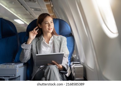 Successful beautiful young asian business woman sits in airplane cabinplane and works on digital tablet with stylus. Flying at first class. - Shutterstock ID 2168585389