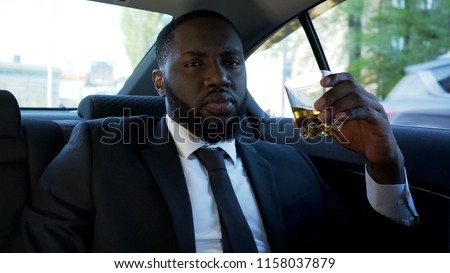 Successful black businessman drinking elite alcohol in car, mafia boss, gangster