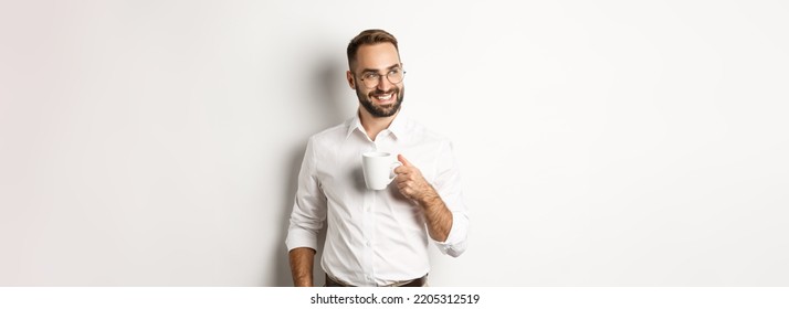 Successful business man drinking coffee, looking sideways with satisfied smile, standing over white background - Powered by Shutterstock