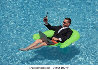 Successful business man floating in suit in pool water. Summer vacations and travel concept. Funny business man drink summer cocktail and using laptop in swimming pool. Summer business concept. - Powered by Shutterstock