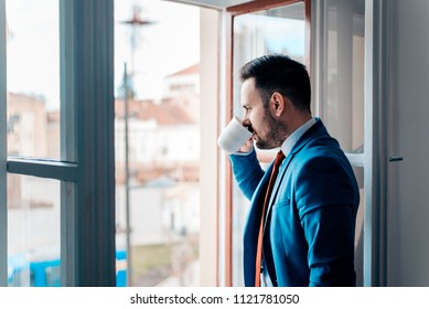 Successful Business Man Looking At City Through Open Window While Drinking From A Cup.