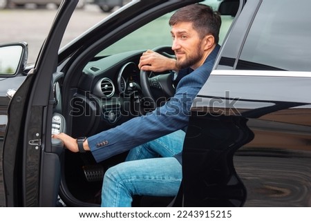 Successful business man with a phone in his hand sits behind the wheel of a prestigious car