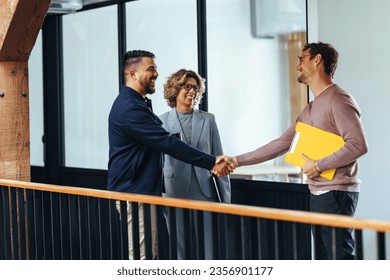 Successful business men shaking hands over a promotion in an office. Happy business professionals reaching an agreement on an internal recruitment deal. - Powered by Shutterstock