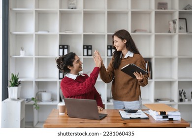 Successful business people giving each other a high five in a meeting. Two young business celebrating teamwork in an office. - Powered by Shutterstock