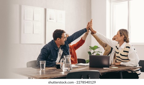 Successful business people smiling and high fiving each other during a meeting in an office. Group of happy designers celebrating their victory as a team in a creative workplace. - Powered by Shutterstock