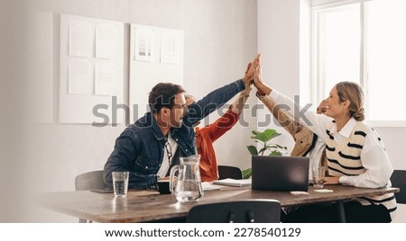 Successful business people smiling and high fiving each other during a meeting in an office. Group of happy designers celebrating their victory as a team in a creative workplace.
