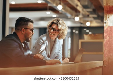 Successful business people working together in a coworking office. Two business professionals working on a tech project. Business colleagues talking to each other.