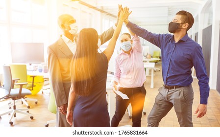 Successful business team with face mask due to corona virus at high five in the office