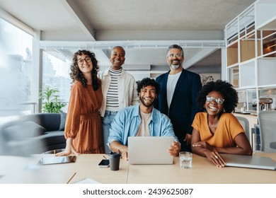 Successful business team working together in an office. They are happy, smiling and looking at the camera, representing their thriving startup company. - Powered by Shutterstock