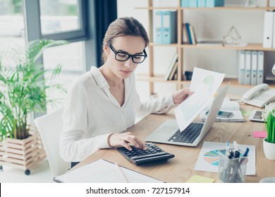 Successful business woman economist in formal wear, sitting at her work place in a light modern design office, making report, in front of laptop, so stylish, concentrated and thoughtful