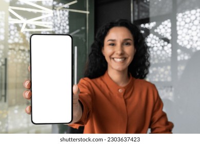 Successful business woman happily shows the smartphone screen to the camera, Latina woman with curly hair at the workplace recommends an online application. - Powered by Shutterstock