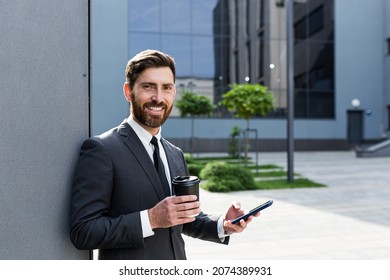 Successful Businessman Broker In A Business Suit Talking On The Phone Near The Office Outside, Banker Holding A Cup Of Coffee During Lunch Break Smiling