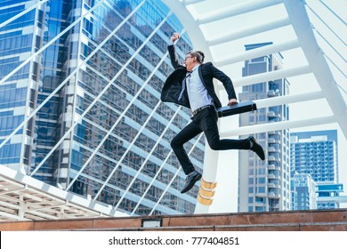 Successful businessman celebrating his victory with jump up in feeling happy on cityscape background. - Shutterstock ID 777404851