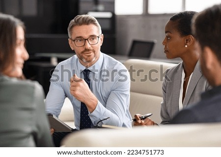 Successful businessman discussing strategy with partners in meeting room. Mature business man entrepreneur in conversation with team in office. Businessman explaining new business ideas to peers.