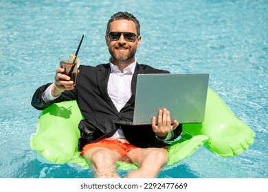 Successful businessman floating in suit in pool water. Summer vacations and travel concept. Funny business man drink summer cocktail and using laptop in swimming pool. Summer business concept.